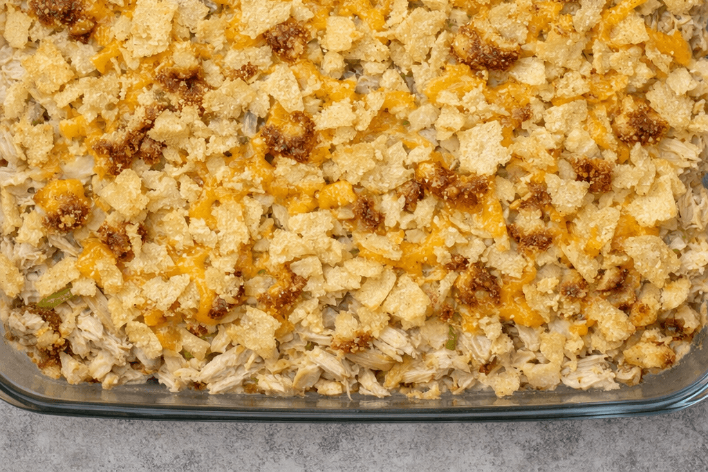 Top‑down photo of Hot Chicken Salad Recipe showing golden potato chips, melted cheese, and creamy chicken filling in a glass dish.