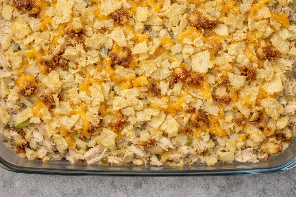 Top‑down photo of Hot Chicken Salad Recipe showing golden potato chips, melted cheese, and creamy chicken filling in a glass dish.