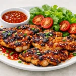 Close‑up of spicy Korean BBQ chicken grilling with glossy gochujang glaze and sesame seeds