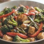 A bowl filled with chicken stir-fry featuring broccoli, red bell peppers, and green onions coated in a glossy brown sauce, showing the final dish prepared using the Chicken Stir-Fry Sauce Formula Recipe.