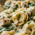 A delicious bowl of Chicken Alfredo Tortellini served on a rustic wooden table with fresh spinach and parmesan